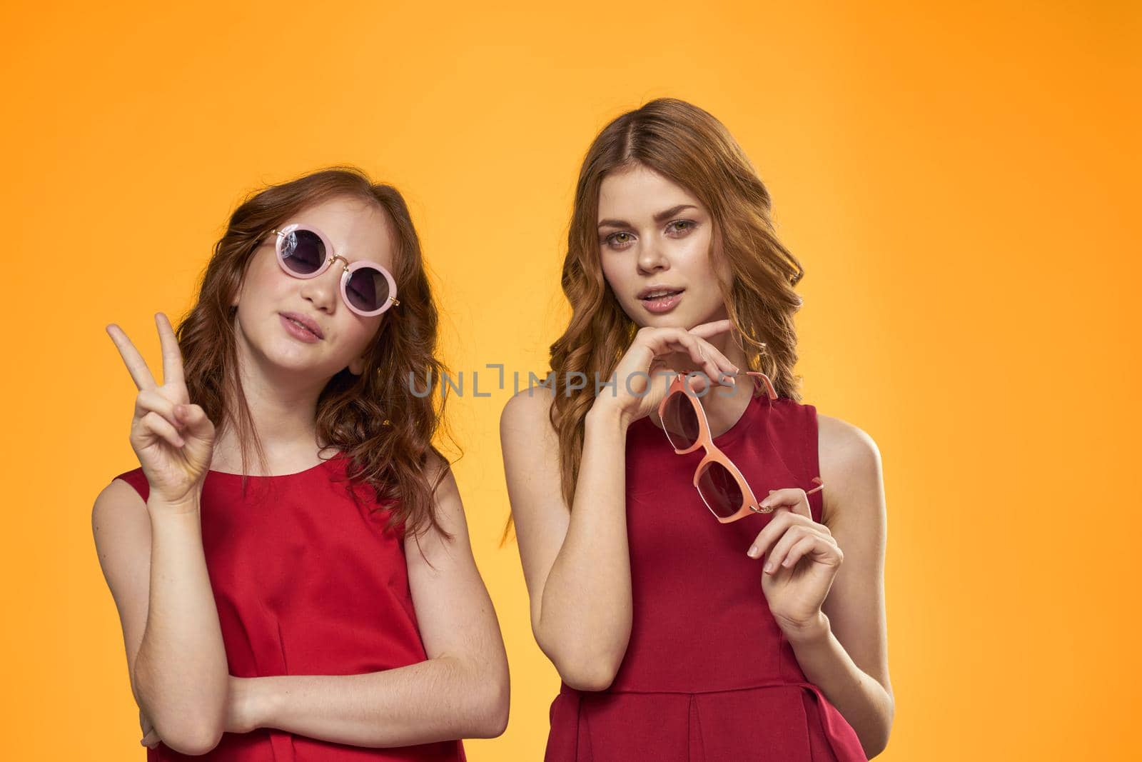 cheerful mom and daughter wearing sunglasses lifestyle friendship family yellow background studio. High quality photo