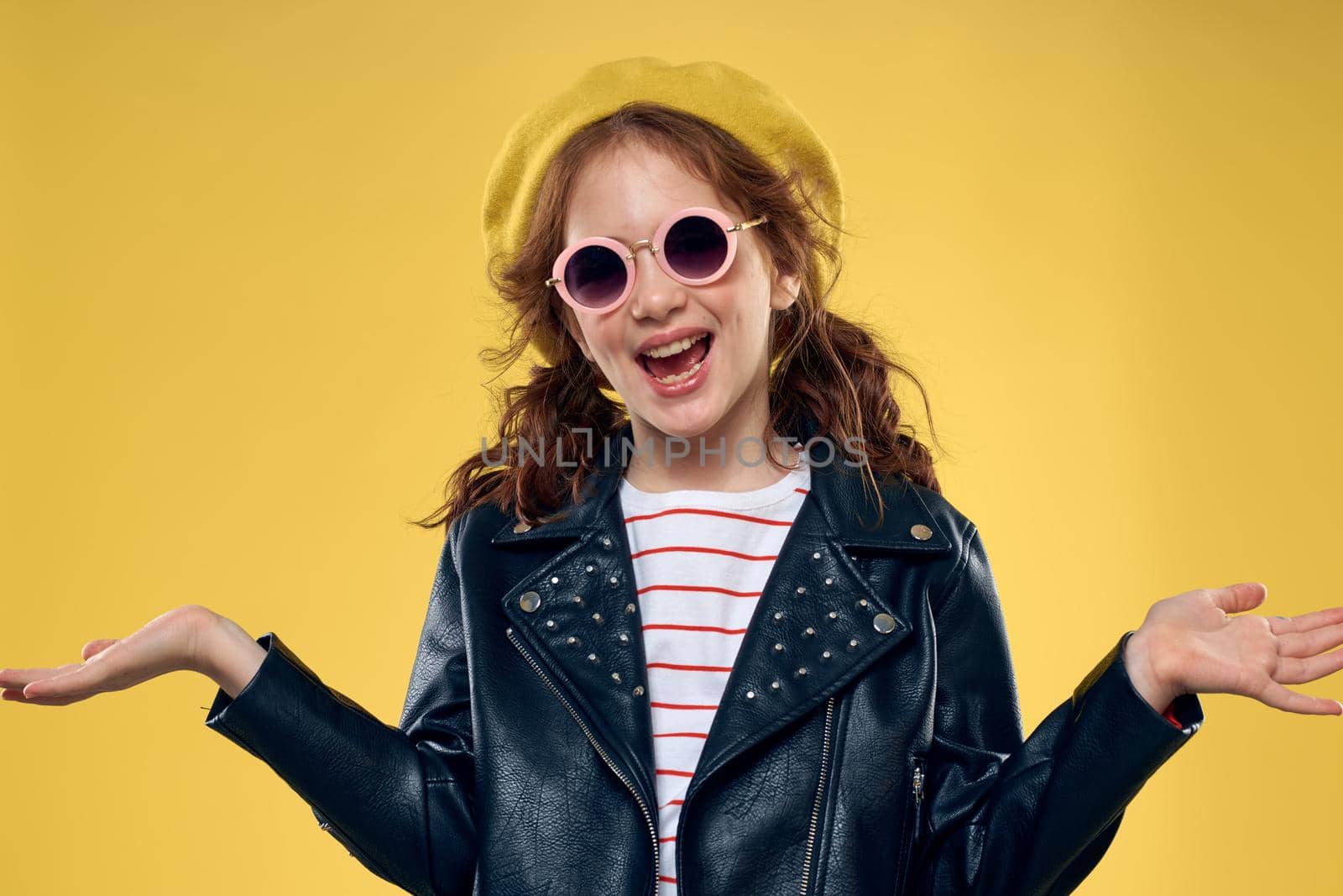 Cheerful little girl in sunglasses and hat lifestyle studio yellow background fashion. High quality photo