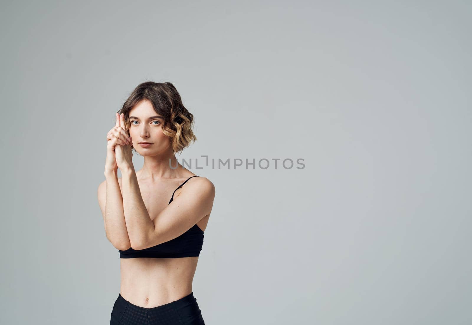 A woman in a short T-shirt on a gray background gestures with her hands to her bare shoulders Fitness Yoga asana by SHOTPRIME