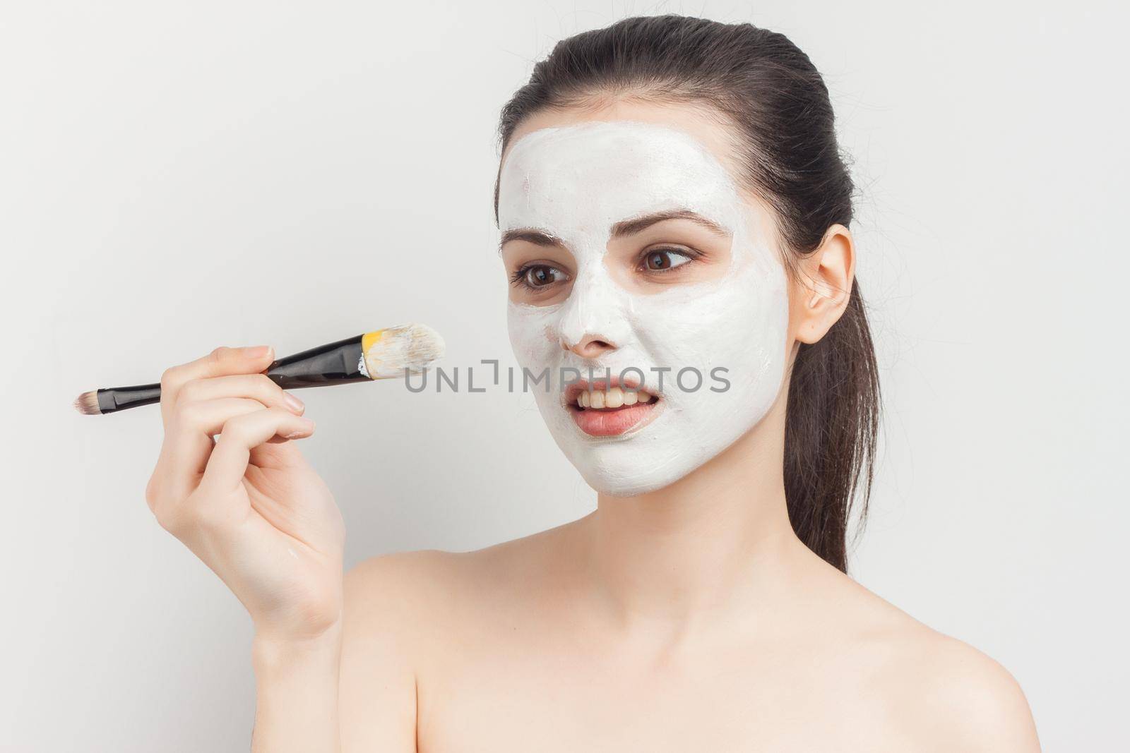 woman with bare shoulders with a brush in her hands applying makeup. High quality photo
