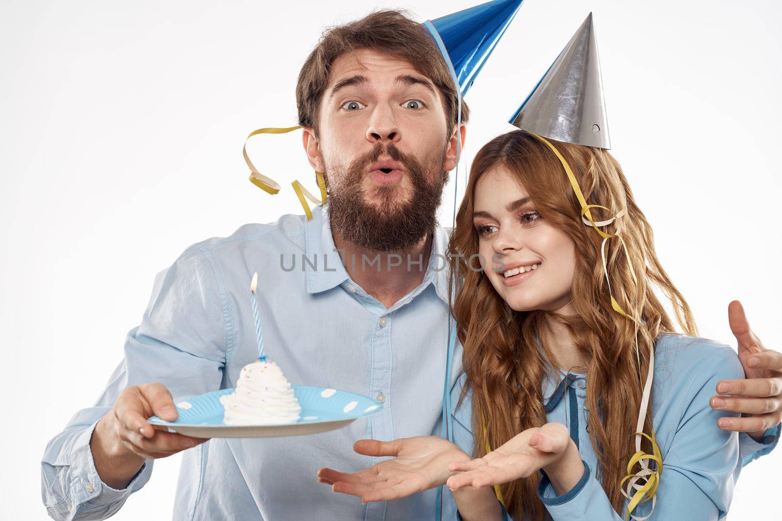 energetic man and woman with a cake and in hats celebrate a birthday on a light background by SHOTPRIME