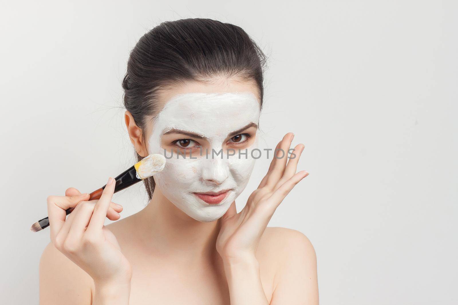 pretty brunette naked shoulders face mask brush in hands skin care procedures. High quality photo