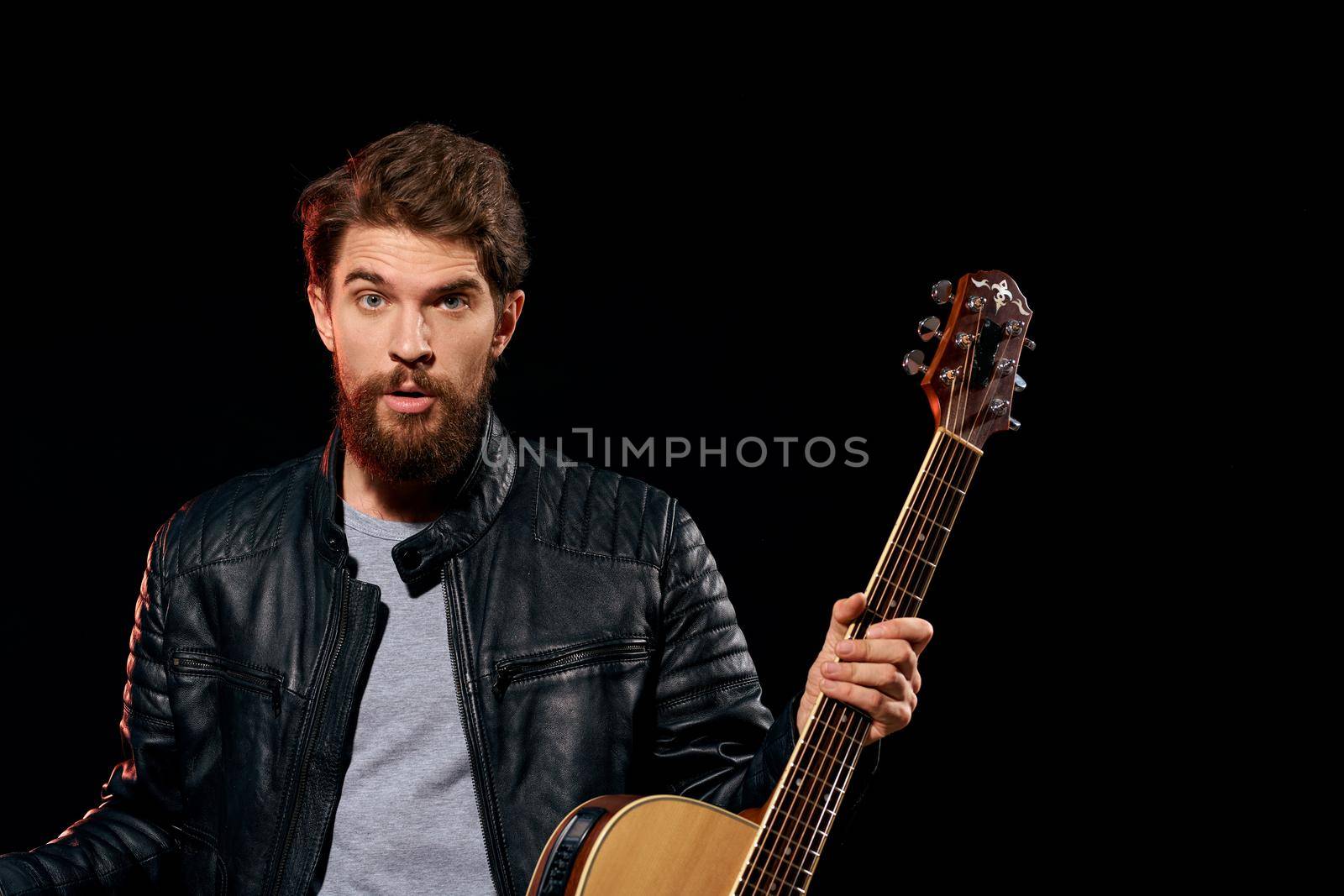 A man with a guitar in his hands leather jacket music performance rock star modern style dark background. High quality photo