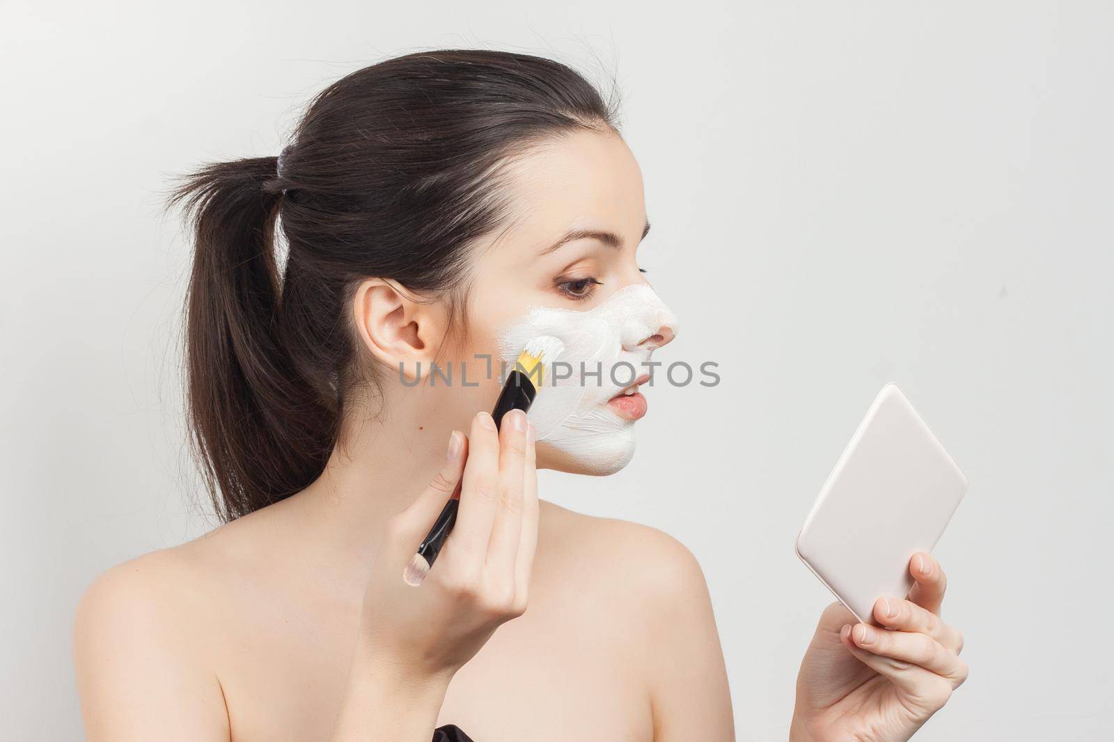 bare-shouldered brunette applying makeup on face cropped view. High quality photo