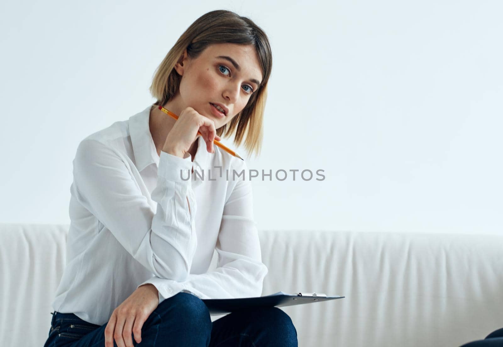 A woman sits on a sofa In a bright room in a shirt and papers . High quality photo