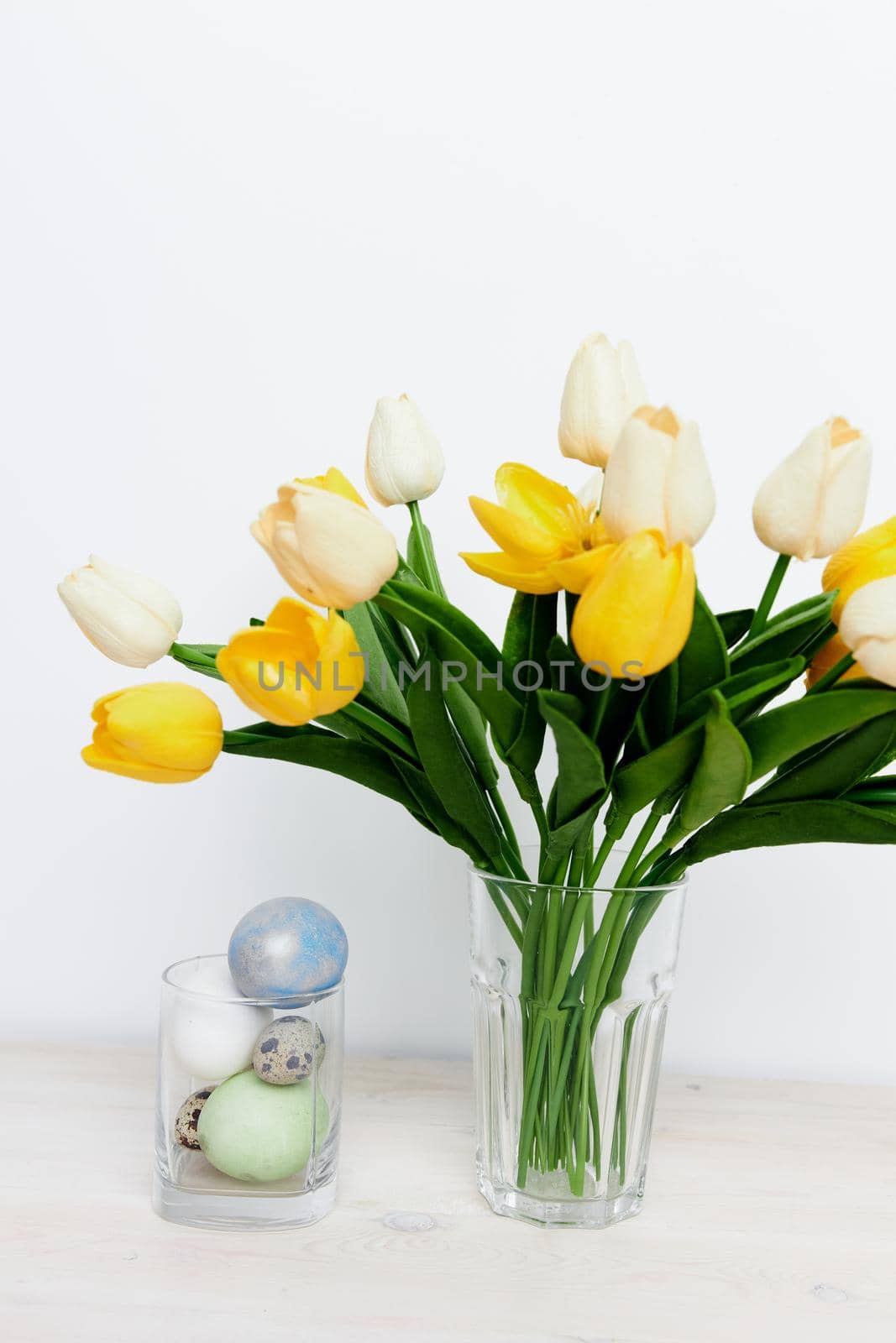 Easter eggs in a glass and yellow tulips in a vase on a light background. High quality photo