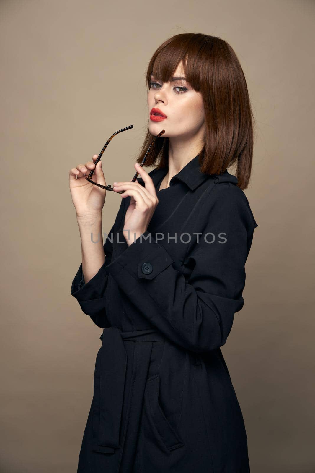 Charming brunette Black coat with bright makeup red lips beige isolated background