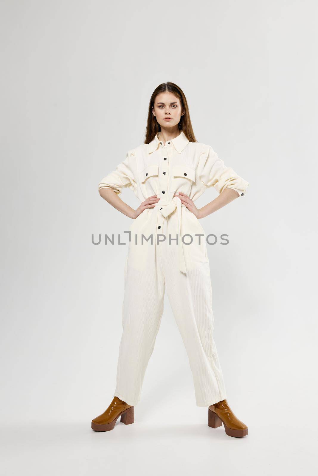 beautiful woman in white jumpsuit holds her hands on the belt and brown shoes. High quality photo