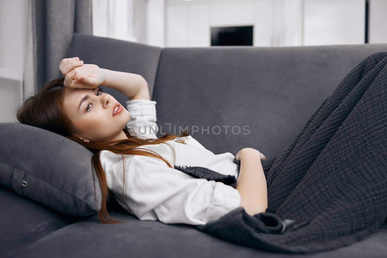 woman lying on the sofa covered with a blanket holds her hand on her head health problems. High quality photo