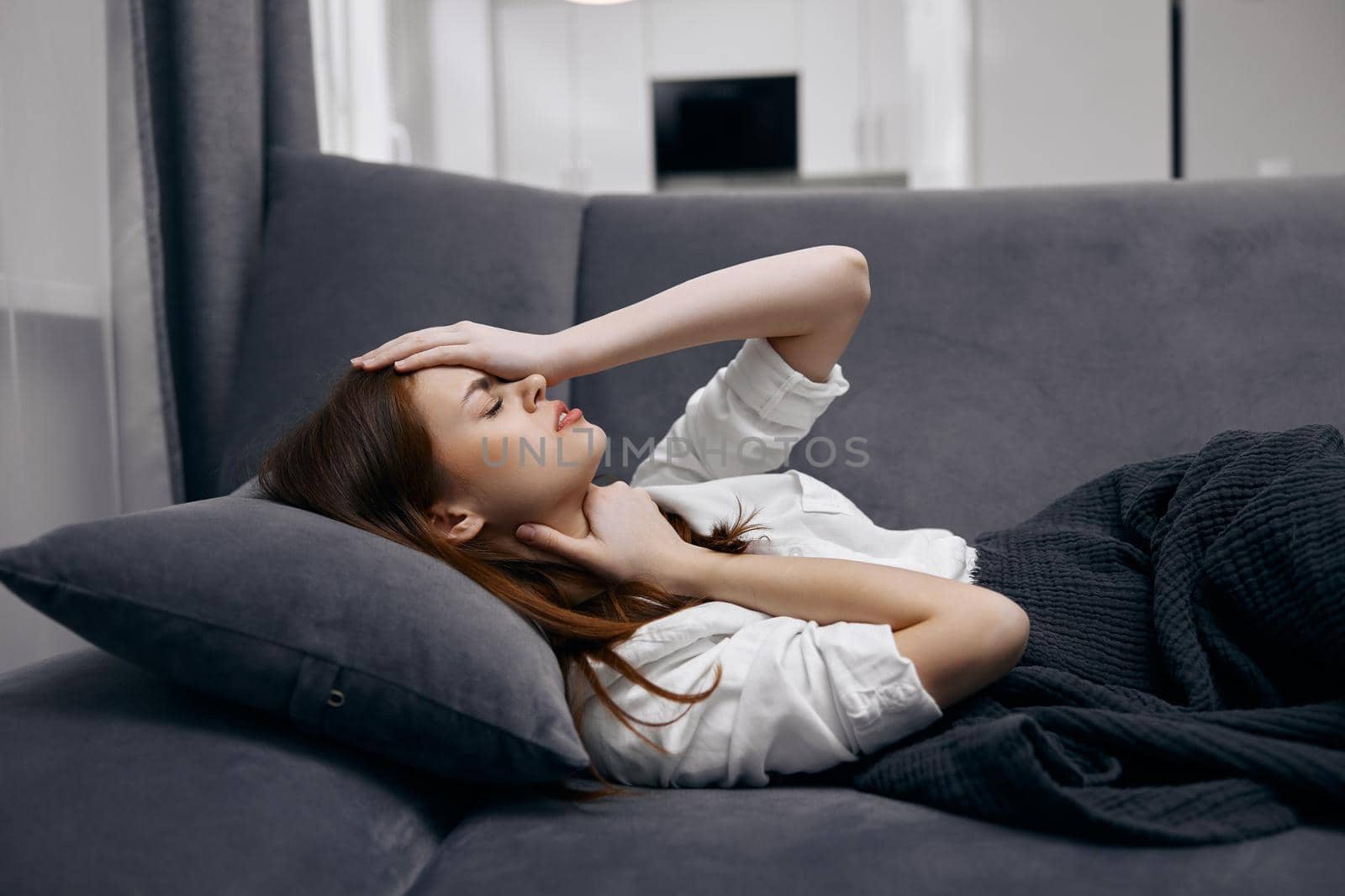 woman at home lies on the sofa covered with a blanket feeling unwell hand on face by SHOTPRIME