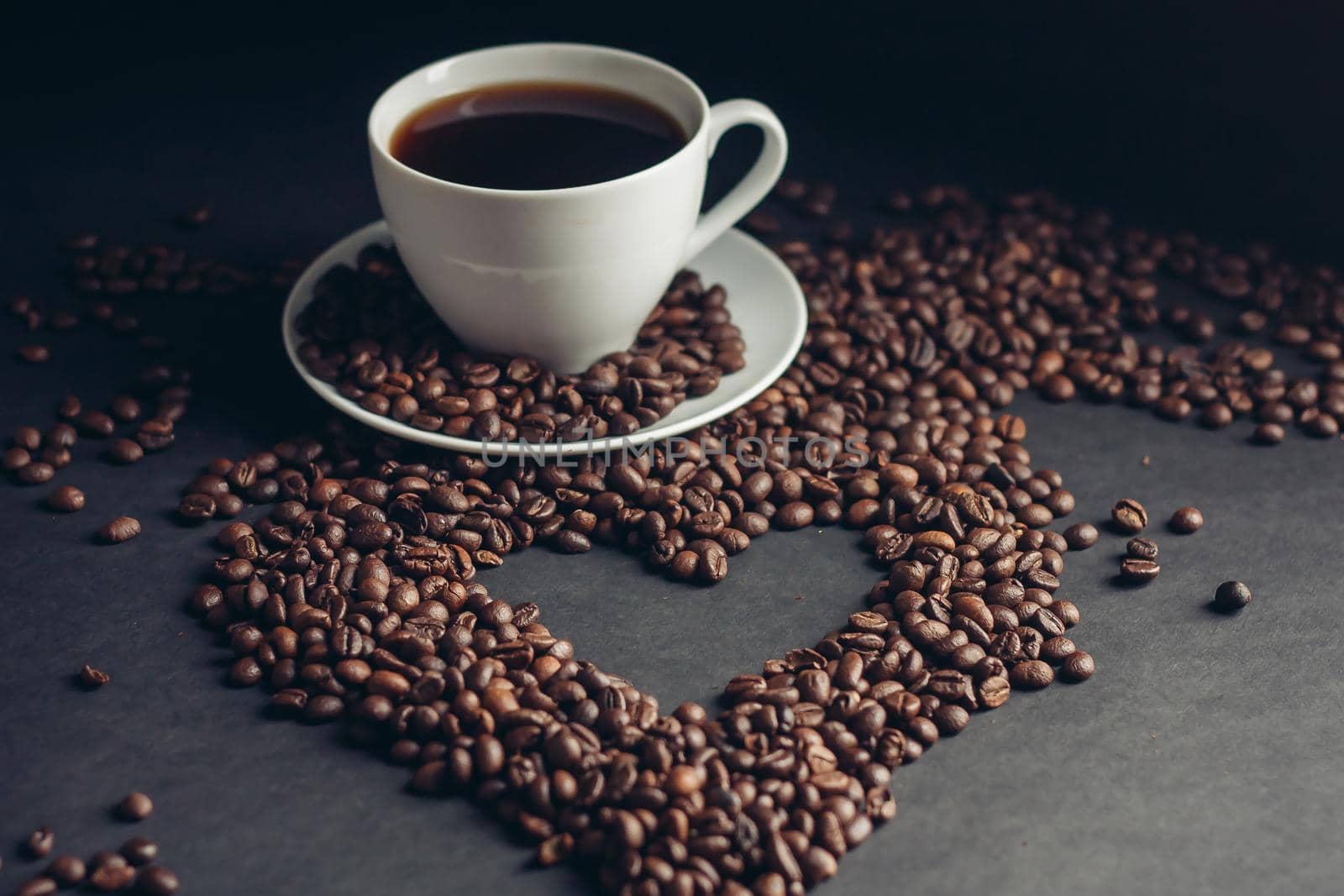 cup with a fragrant drink on a dark background heart of coffee beans white saucer. High quality photo
