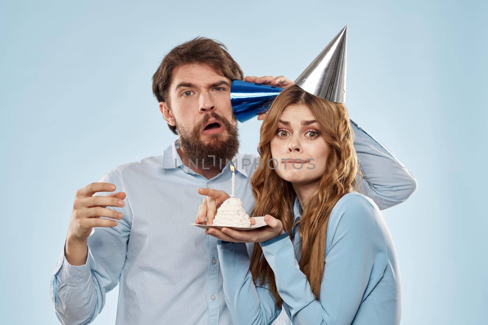 Cheerful man and woman blowing out cake candles holiday decoration blue background. High quality photo