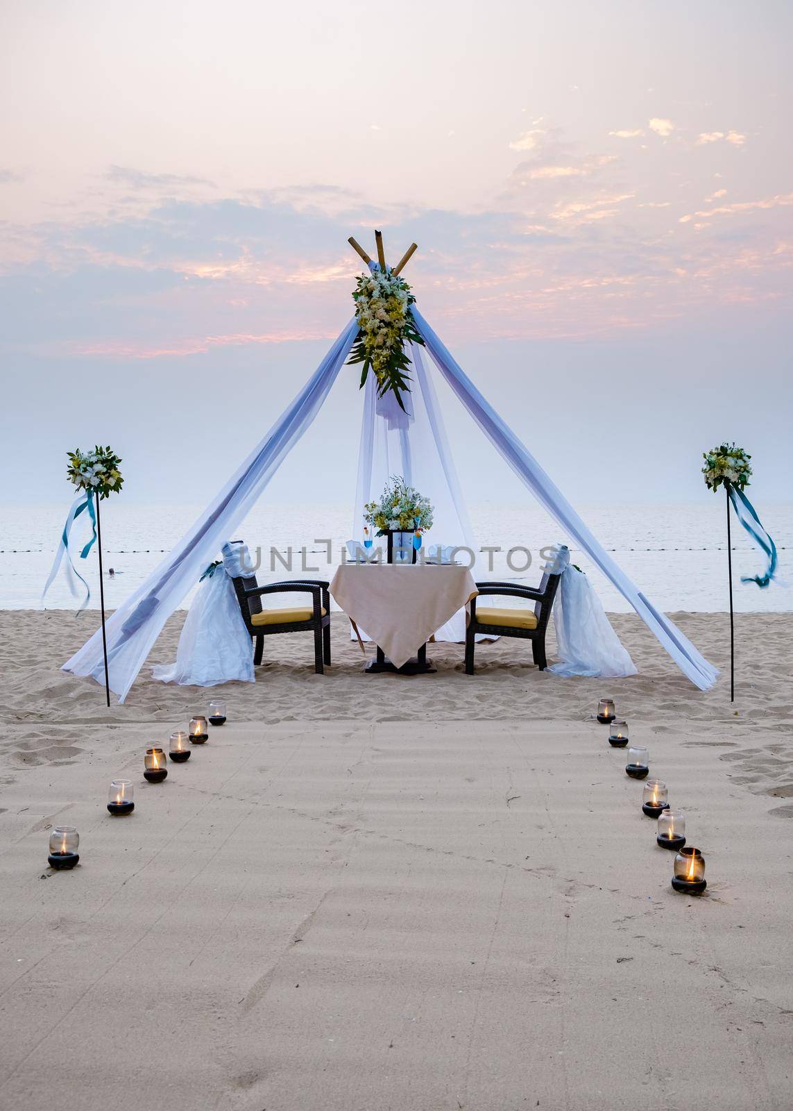 Loving couple share a romantic dinner with candles, lanterns and wine glasses at sea beach sand against wonderful sunset by fokkebok