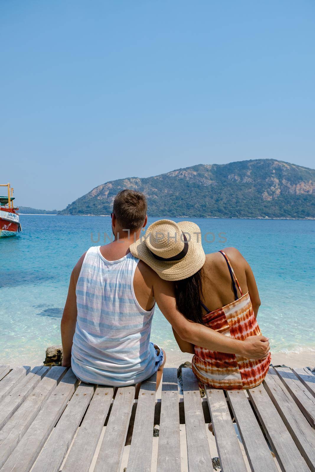 A couple from behind on the backside looking out over the ocean of tropical Island, men and woman vacation, beautiful tropical island beach Koh Kham, Trat Thailand couple relax on tropical Island. 