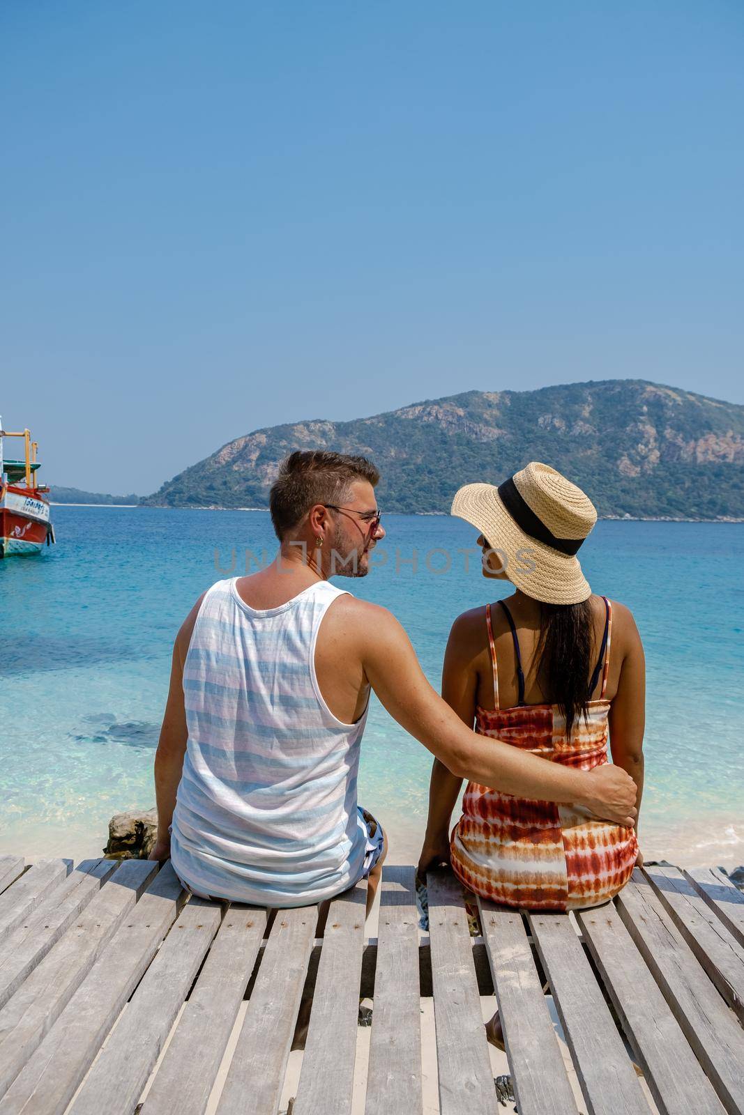 A couple from behind on the backside looking out over the ocean of tropical Island, men and woman vacation, beautiful tropical island beach Koh Kham, Trat Thailand couple relax on tropical Island. 