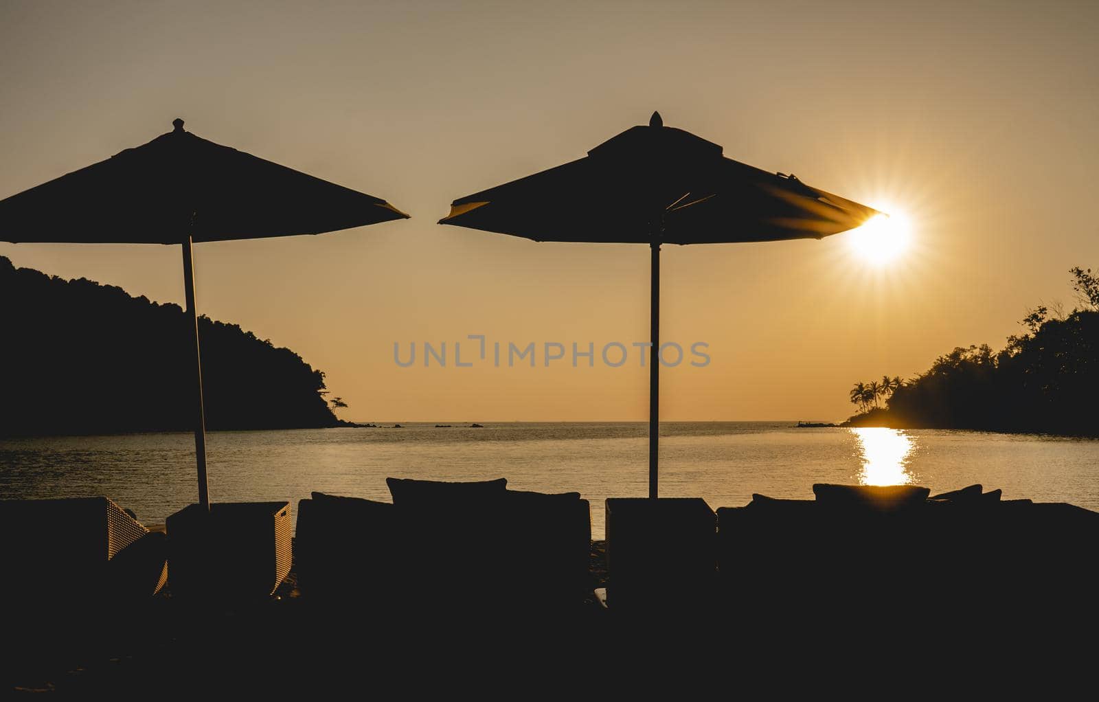 Sunset ocean view. Sun above the sea on orange sky, umbrella and chair nearly beach.