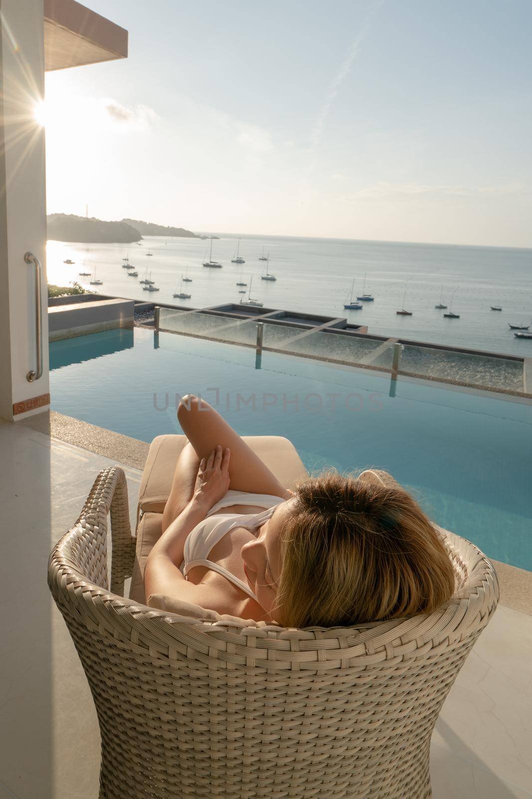 Woman lying on day bed in the balcony with pool and seaside view.
