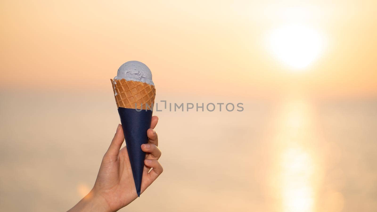Scoop ice cream with a waffle cone in hand on the beach, sunset moment.