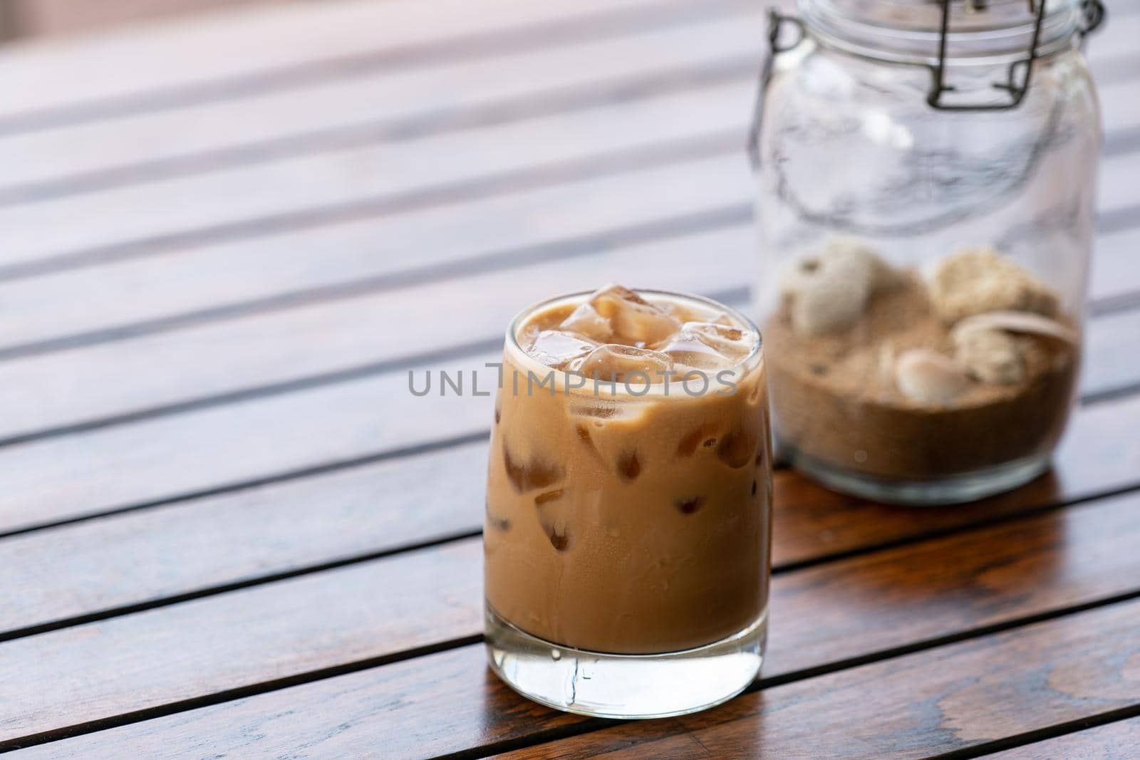 Glass of iced coffee with sand in bottle lamp on wooden table.