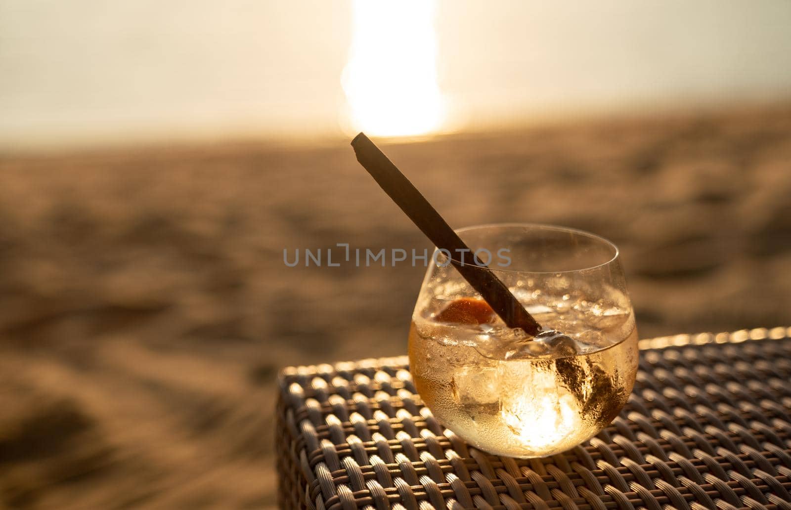 Ice cocktail glasses with cinnamon straws on wooden table over sea sunset. by sirawit99