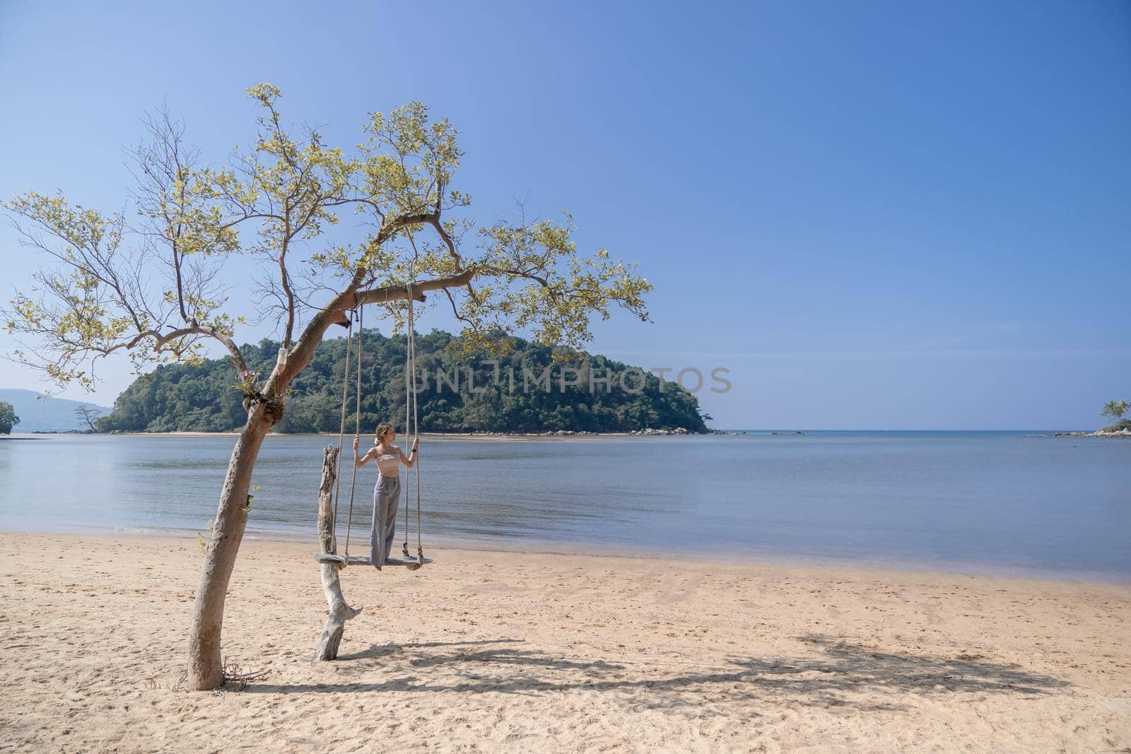 Woman standing on a swing, on the beach.