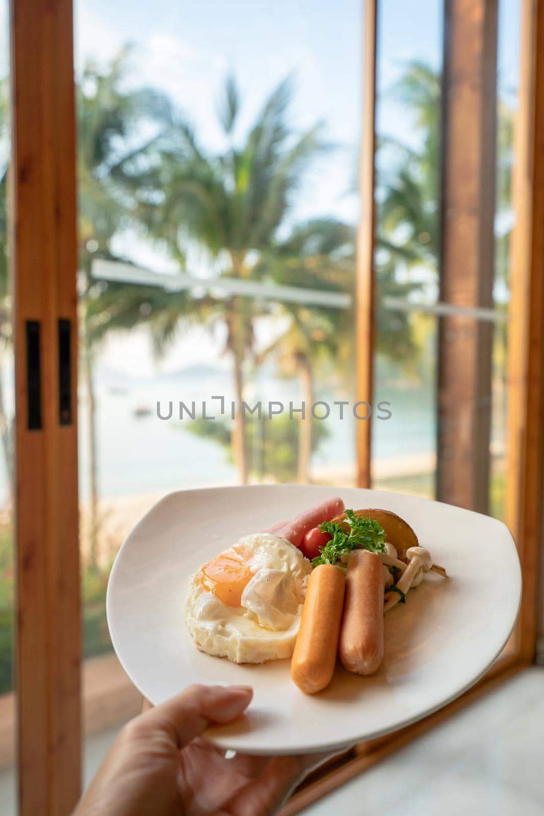 hand holding American breakfast set with fried eggs grill sausage and vegetable salad on beach background in morning.