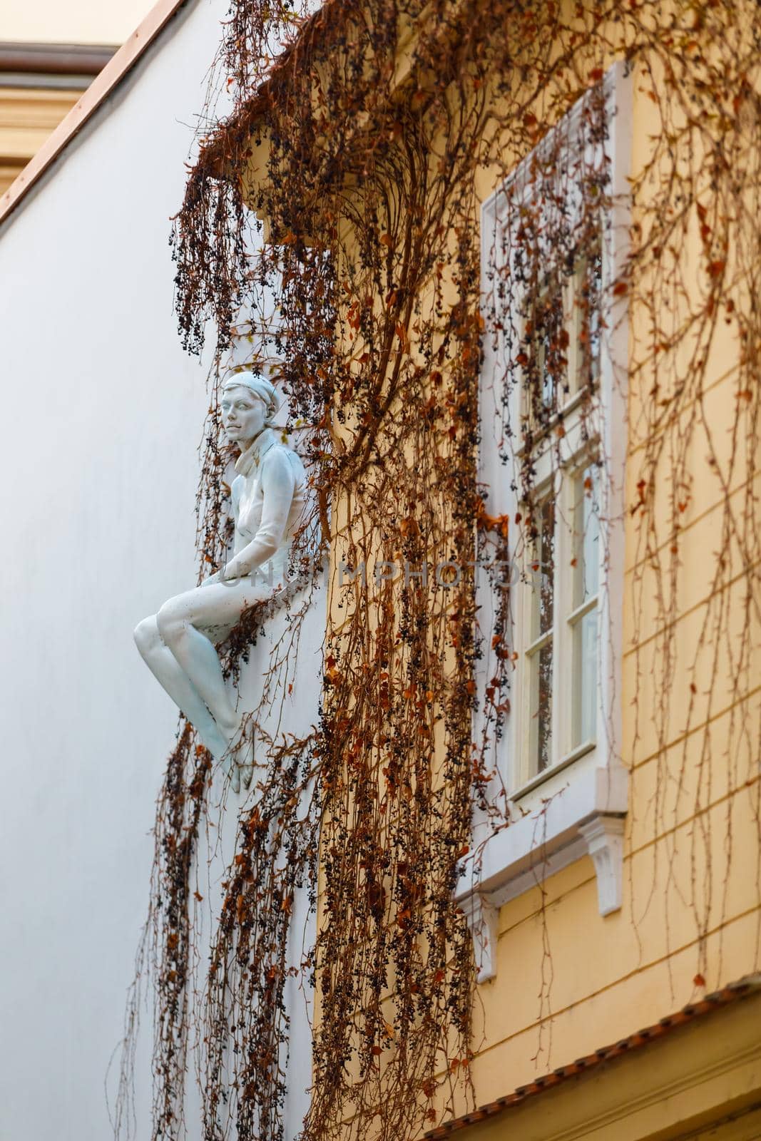 Prague, Czech Republic April 14, 2018. Sculpture of a girl sitting on the edge of the building's roof. Plants grow on the wall.