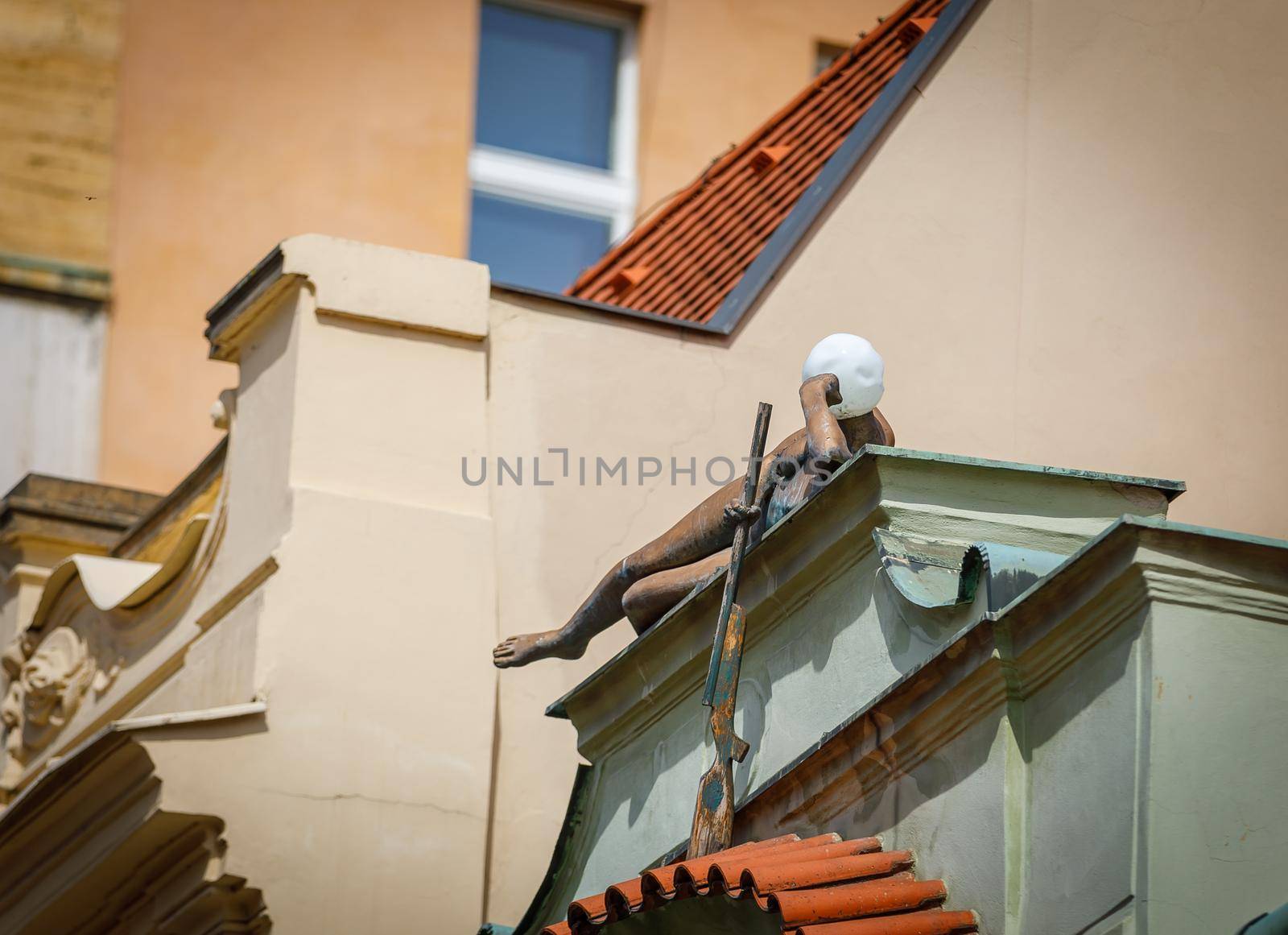 Prague, Czech Republic, April 14, 2018. A sculpture of a naked girl lying on the edge of the roof of a building with a gun. Instead of a head, a lantern