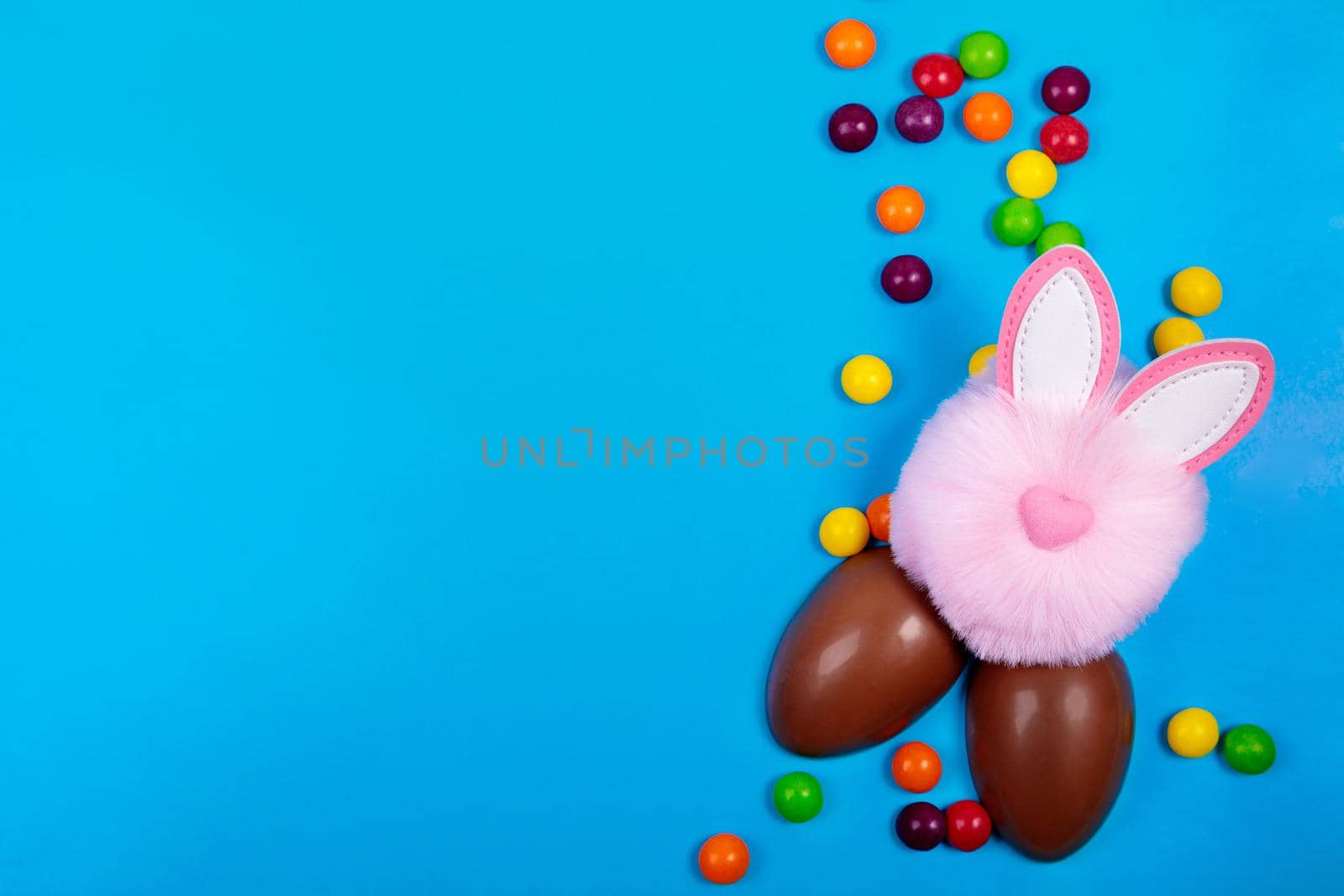 Easter concept, candy jelly beans, chocolate egg, pink rabbit head toy on a blue background. Place for text