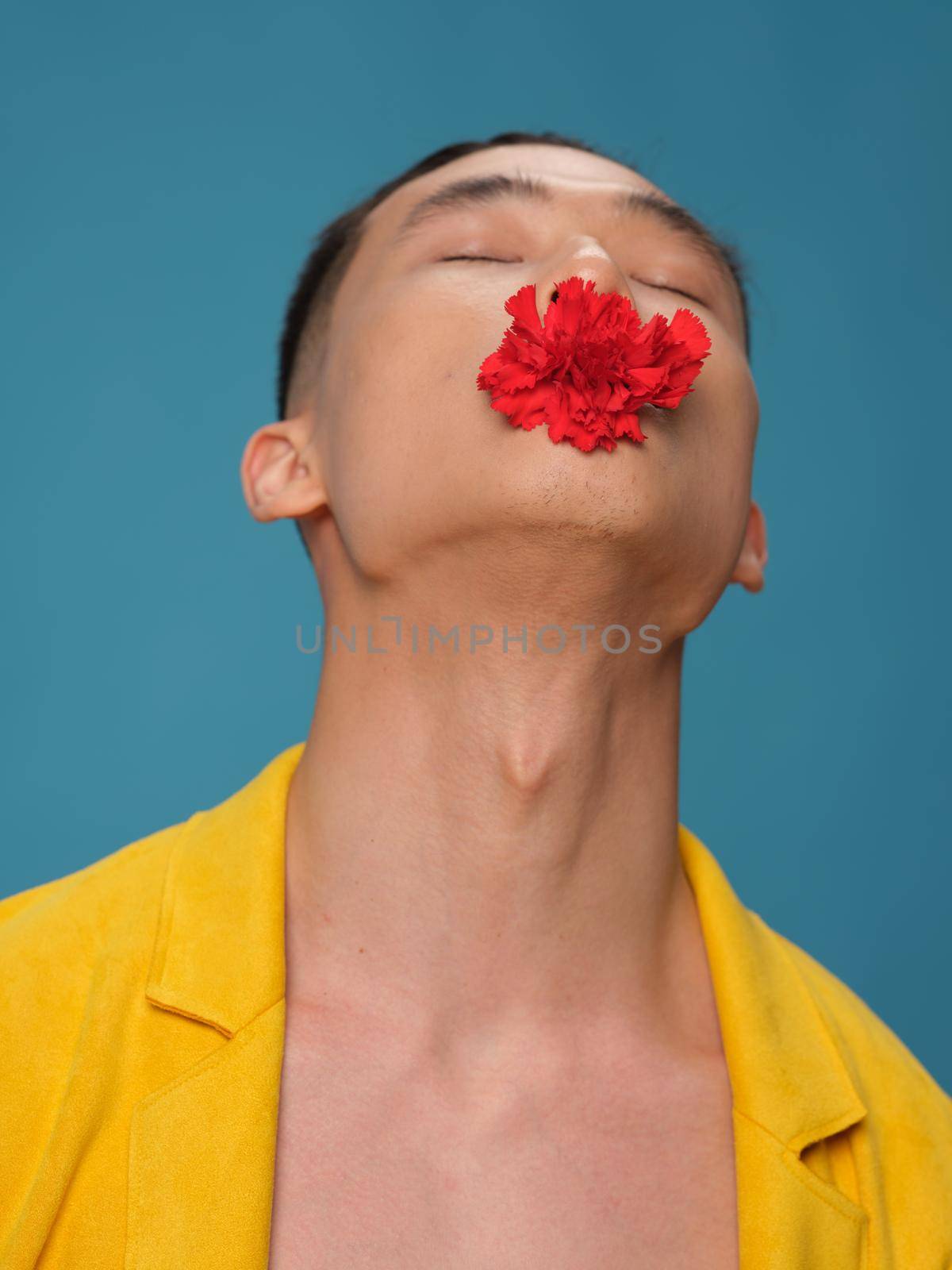 Asian man tilted his head back and flower in mouth blue background. High quality photo