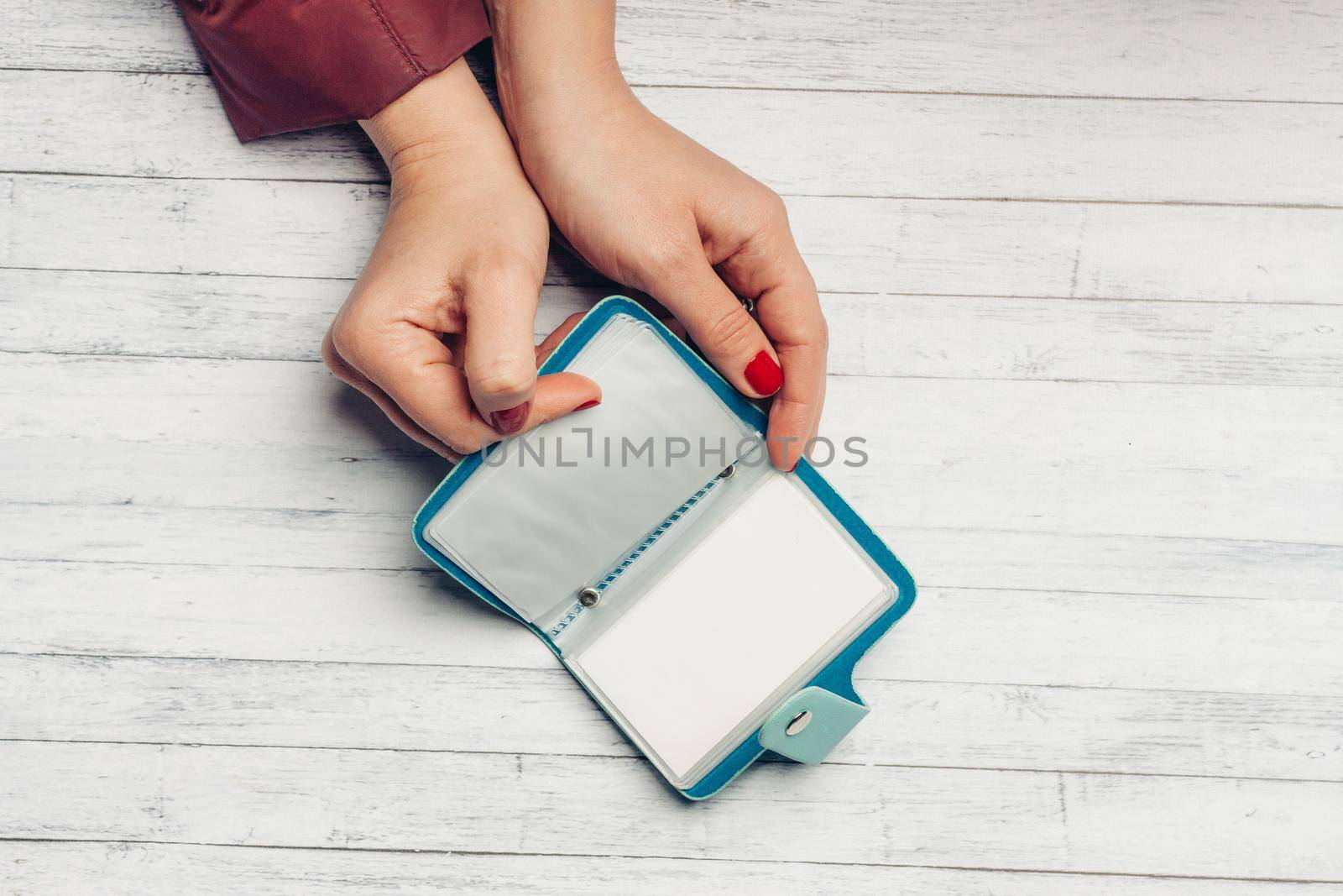 blue card holder in female hands and white sheet of paper wooden background texture. High quality photo