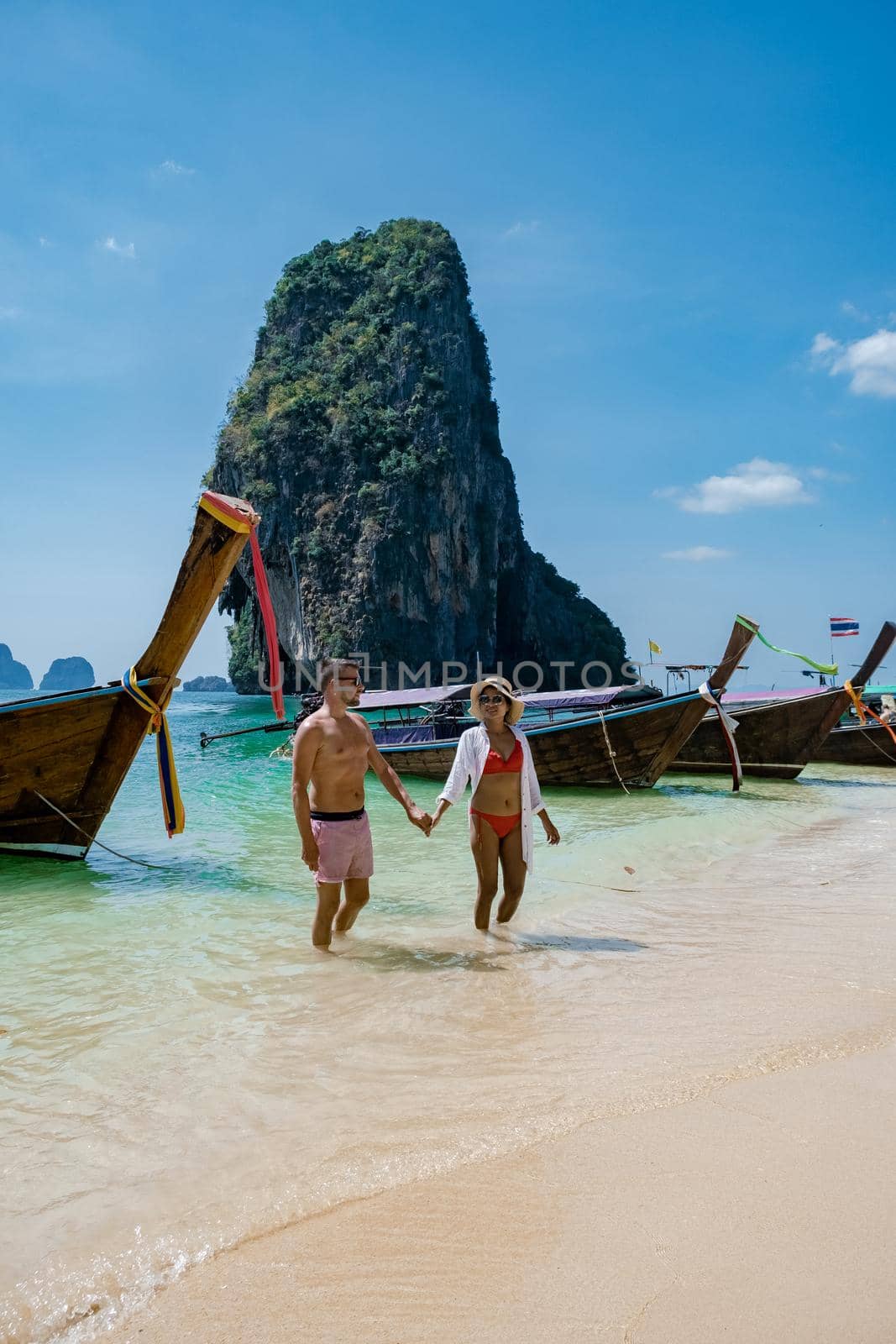 couple mid age on tropical beach in Thailand, tourist walking on a white tropical beach, Railay beach with on the background lontail boat drop off tourist by fokkebok