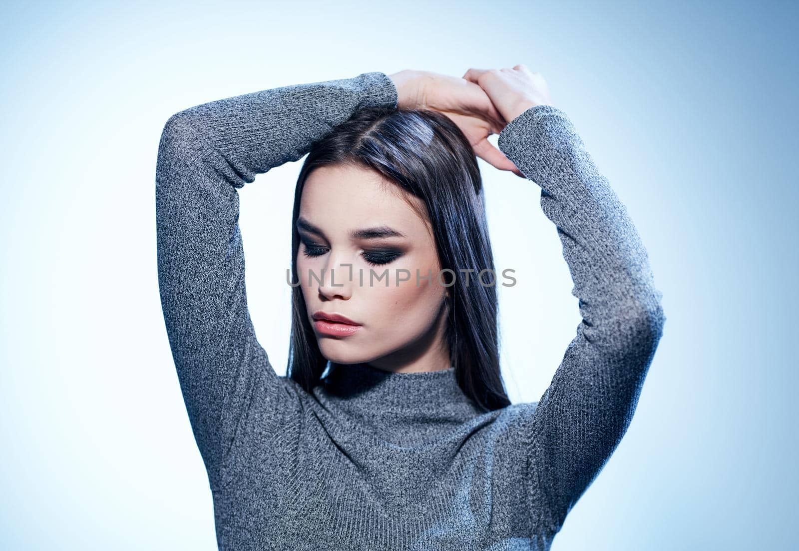 Sexy brunette in a gray sweater on a light background holds her hands behind her head cropped view. High quality photo