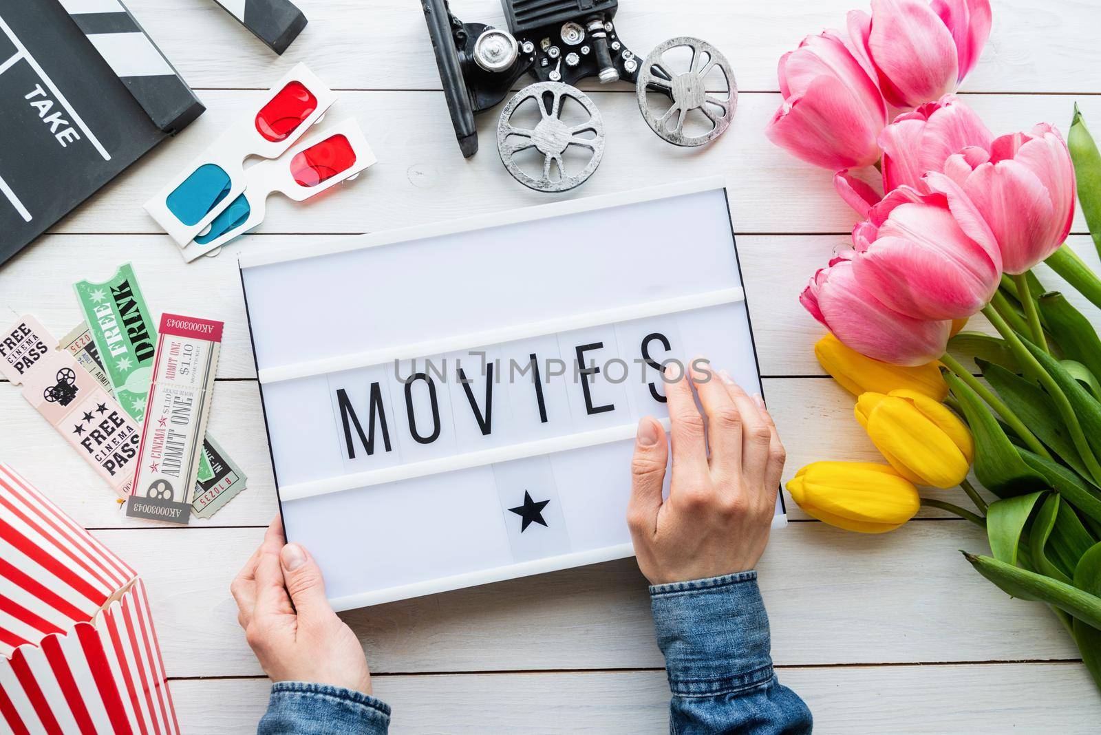 Retro and vintage. Top view of woman hands holding lightbox with word Movies, clapper board, tickets, tulips and 3D glasses , top view flat lay