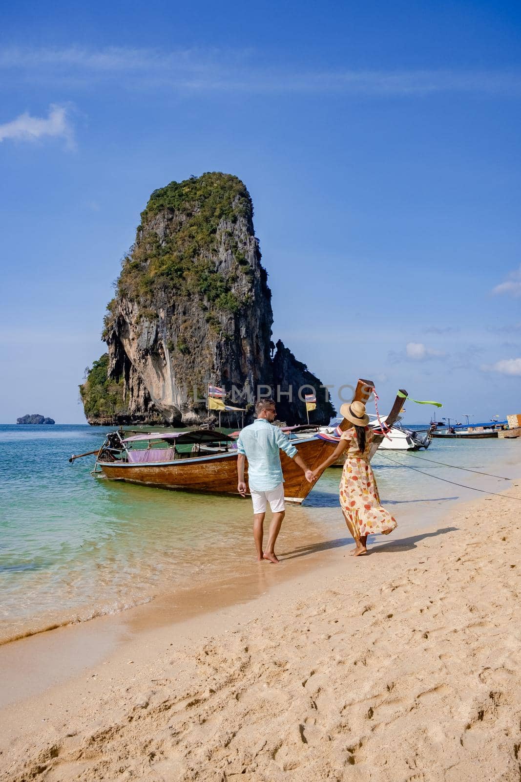 couple mid age on a tropical beach in Thailand, tourist on a white tropical beach, Railay beach with on the background longtail boat. Railay Beach in Krabi province. Ao Nang, Thailand.