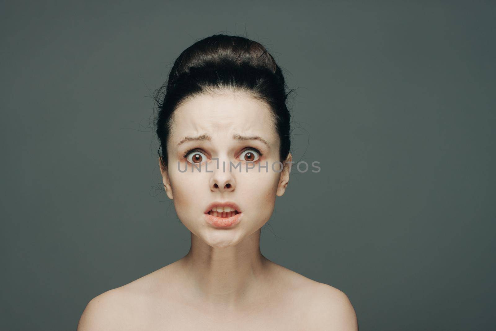 portrait of a woman with bare shoulders emotions gathered hair in a bun gray background by SHOTPRIME