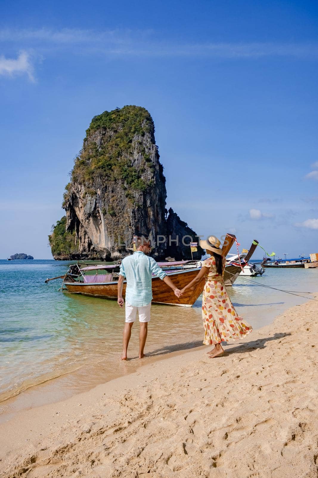 couple mid age on a tropical beach in Thailand, tourist on a white tropical beach, Railay beach with on the background longtail boat. Railay Beach in Krabi province. Ao Nang, Thailand.