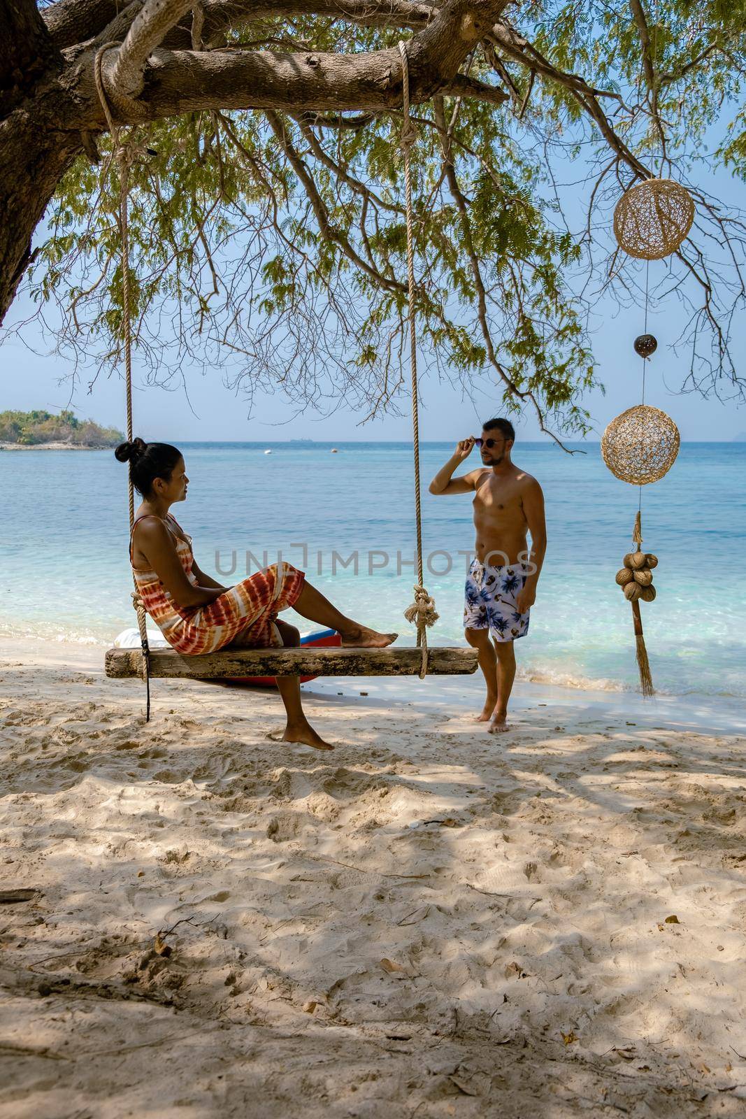 A couple from behind on the backside looking out over the ocean of tropical Island, men and woman vacation, beautiful tropical island beach Koh Kham, Trat Thailand couple relax on tropical Island. 
