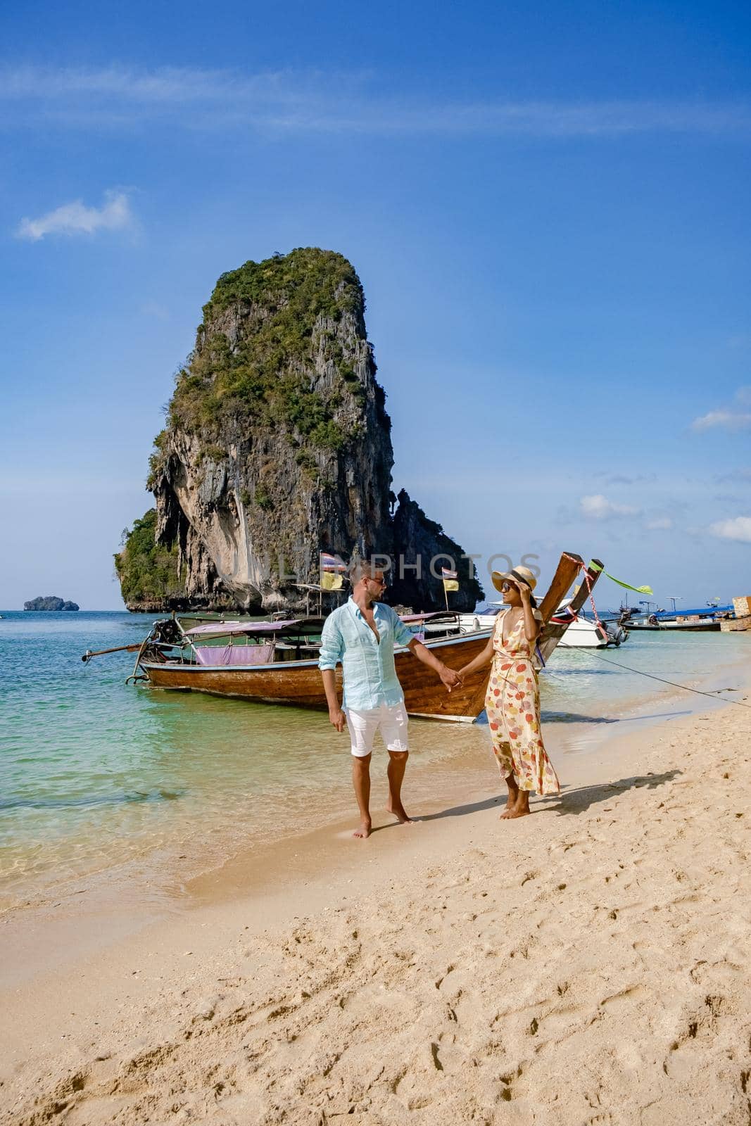 couple mid age on a tropical beach in Thailand, tourist on a white tropical beach, Railay beach with on the background longtail boat. Railay Beach in Krabi province. Ao Nang, Thailand.