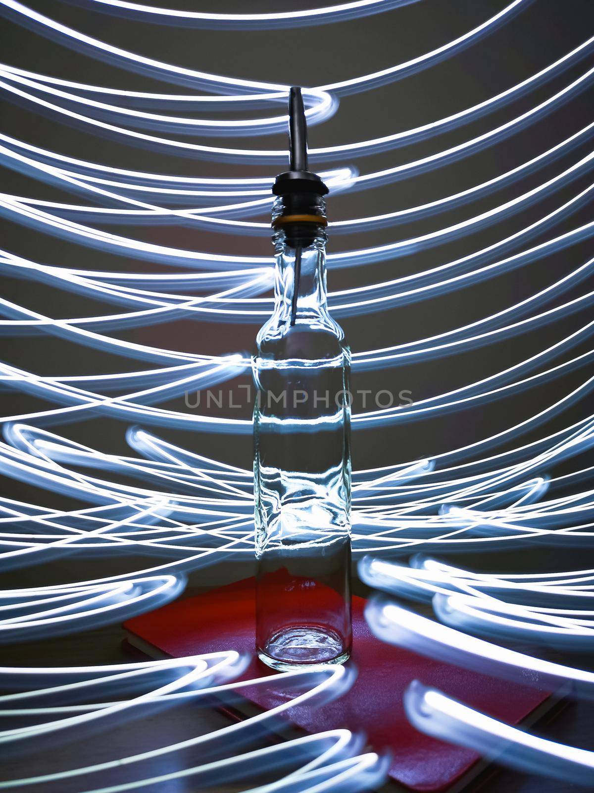 Small narrow bottle with bartender pourer on table with light paiting around