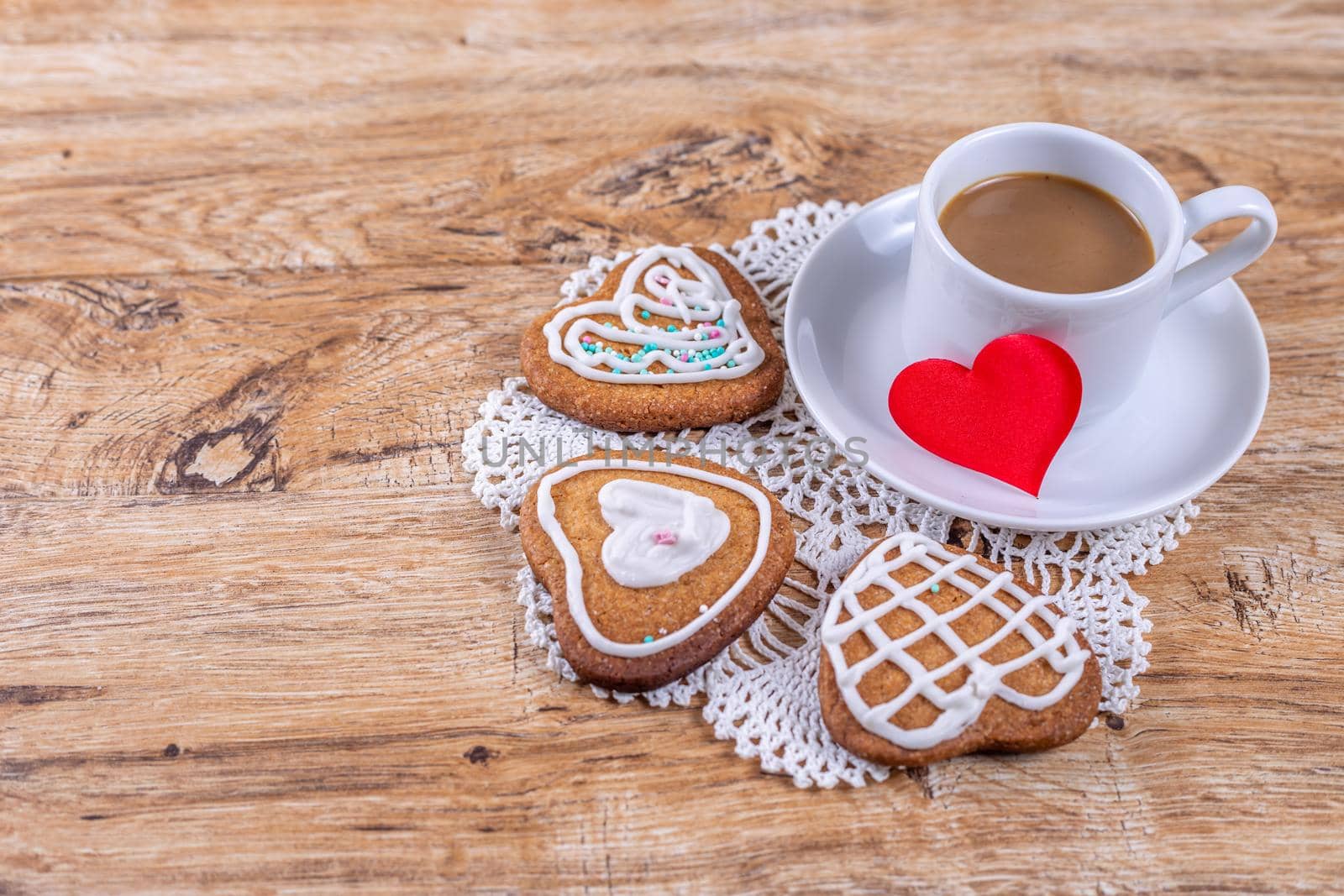 Homemade heart-shaped cookies, decorated with white icing with decorative sprinkles, and red hearts on a wooden table with a cup of coffee, top and side view.