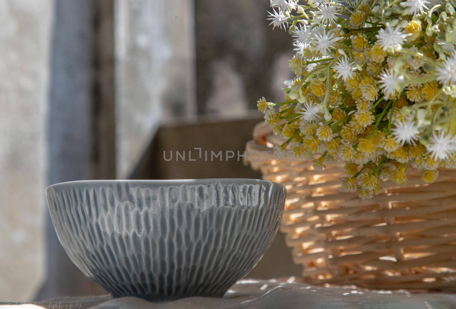 Ceramic bowl and bouquet of flowers in woven basket on white textured table cloth. Selective focus.