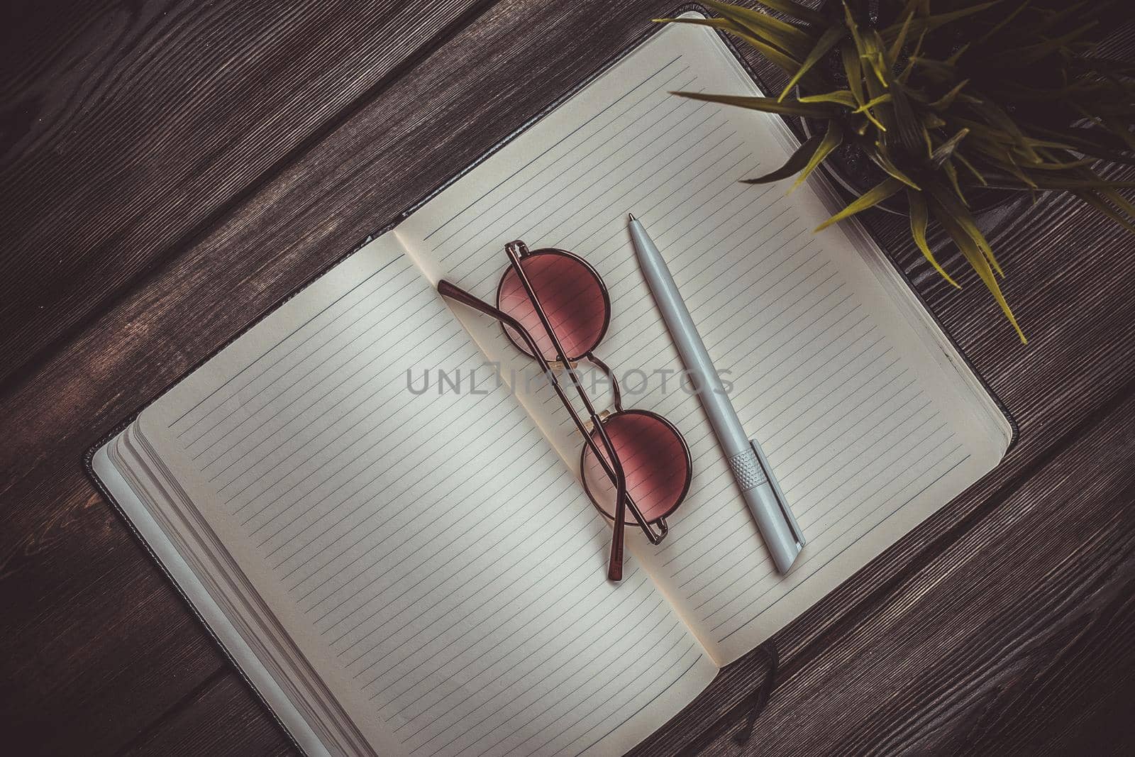 notepad glasses and a flower in a pot on a wooden table top view pen office. High quality photo