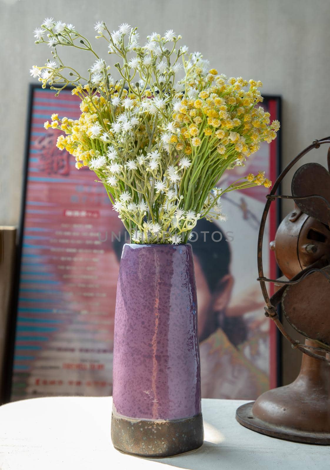 Bouquet of flowers in Purple ceramic vase on white textured table cloth in front of Classic chinese poster movie frame with old cement wall. Home decor, Selective focus.