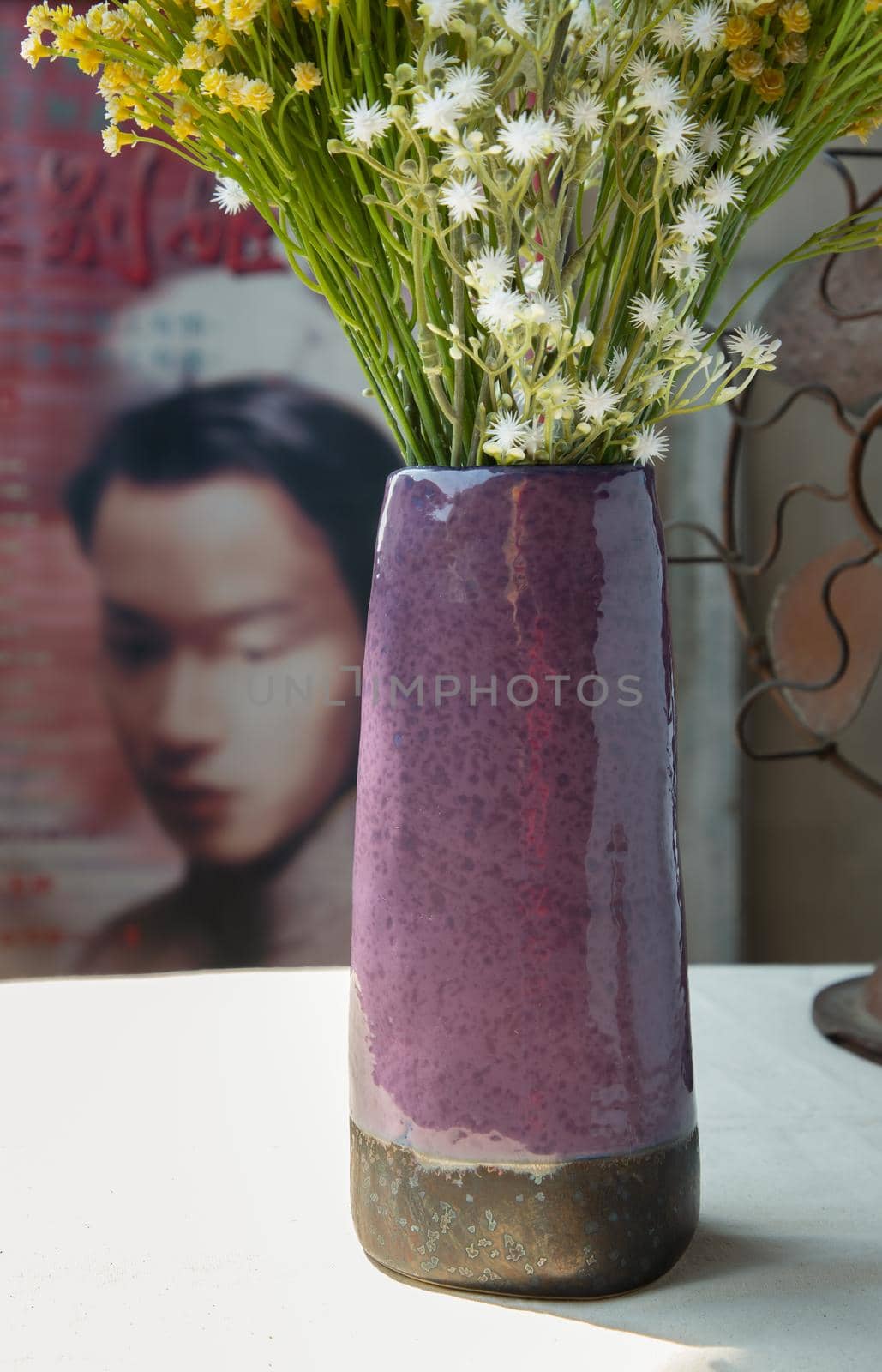 Bouquet of flowers in Purple ceramic vase on white textured table cloth in front of Classic chinese poster movie frame with old cement wall. Home decor, No focus, specifically.