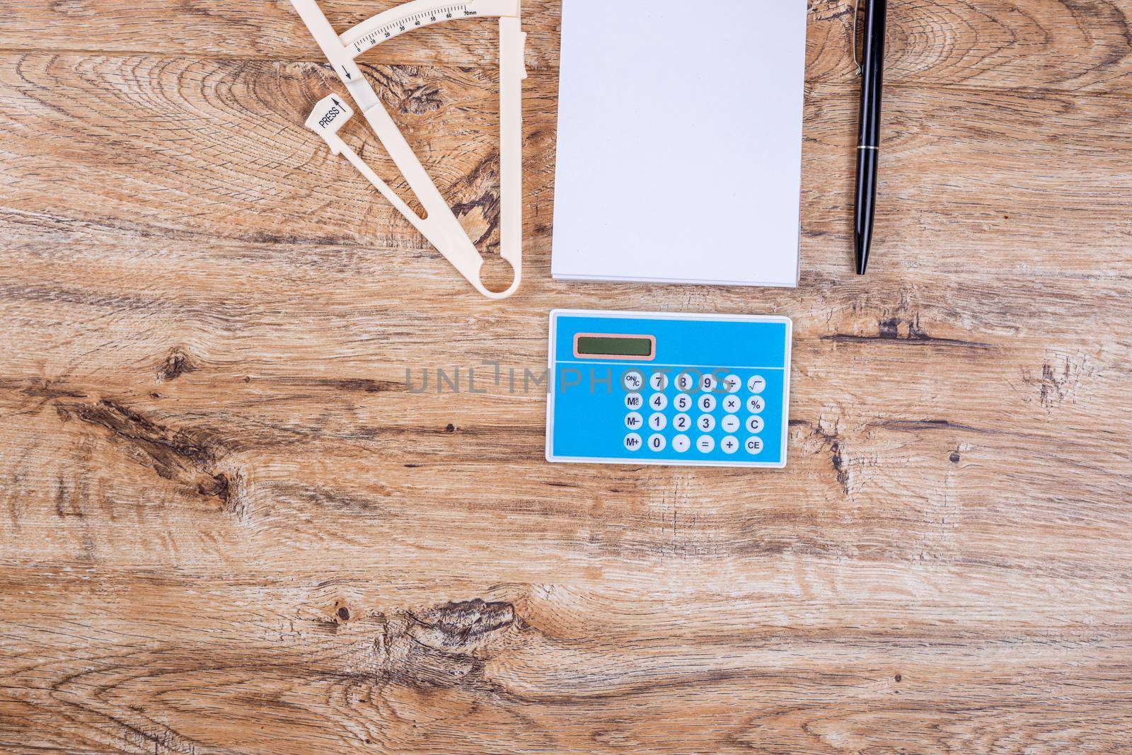Blank sheet of notepad pen calculator and caliper on wooden table top view layout. The concept of proper nutrition, calorie counting, weight loss.