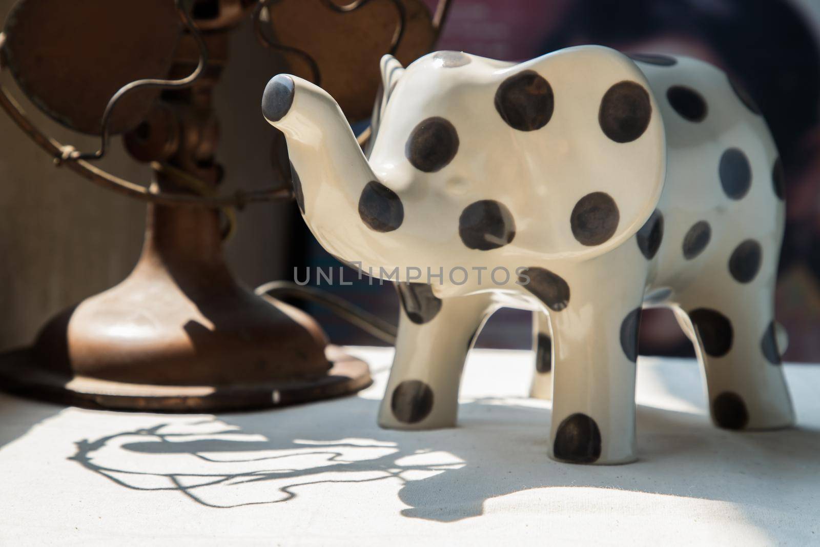 Elephants shaped ceramic and Vintage metal fan on white textured table cloth. Home decor, No focus, specifically.