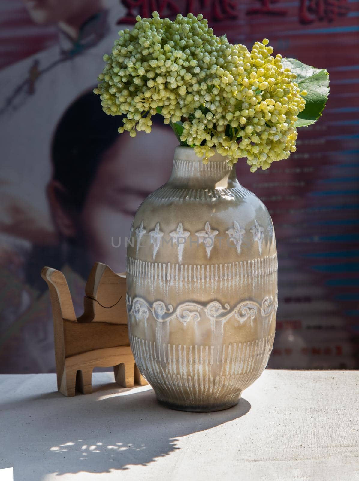 Bouquet of flowers in Beautiful ceramic vase and Wooden doll cat shape on white textured table cloth in front of Classic chinese poster movie frame. Home decor, No focus, specifically.