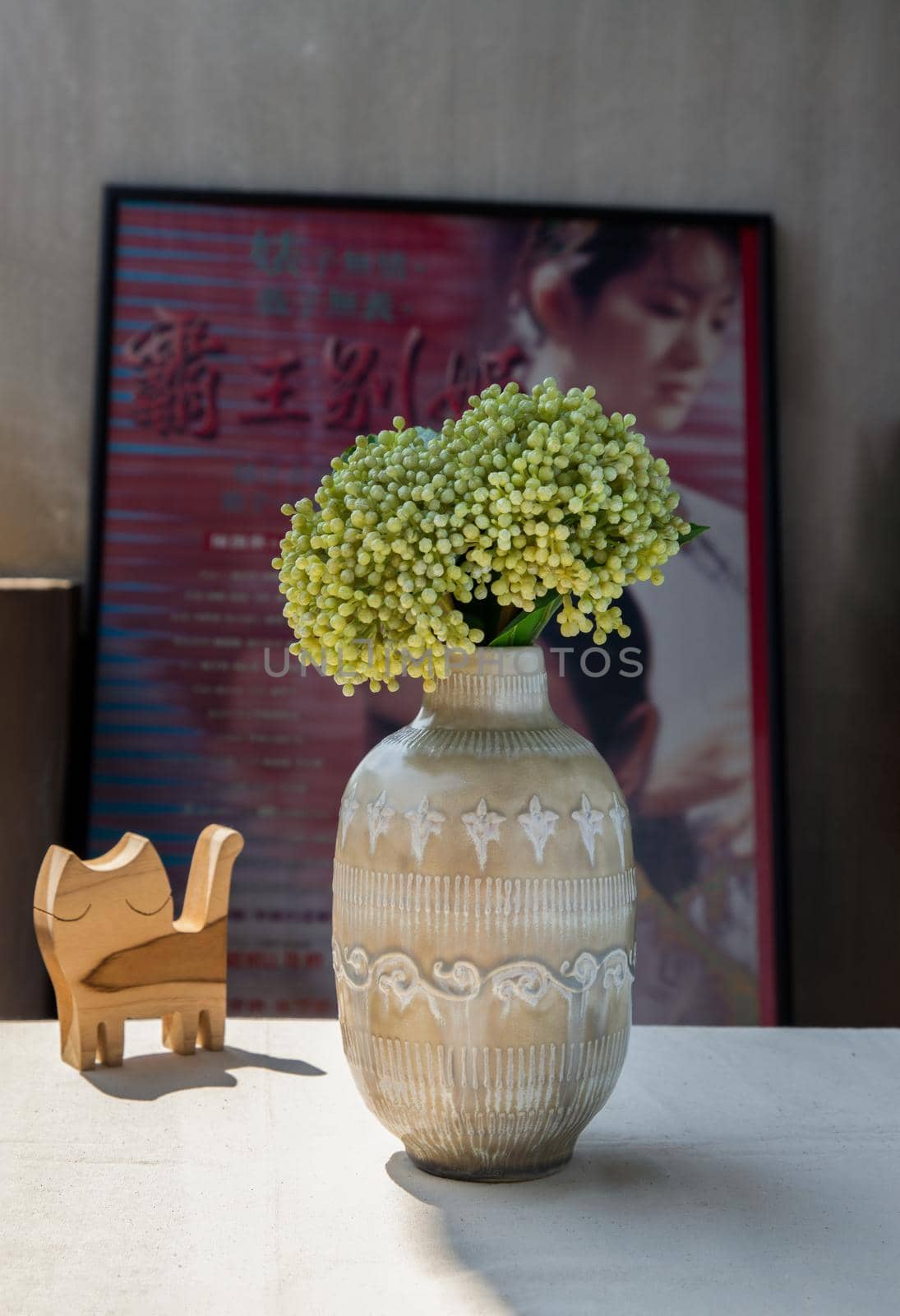 Bouquet of flowers in Beautiful ceramic vase and Wooden doll cat shape on white textured table cloth in front of Classic chinese poster movie frame with old cement wall. Home decor, Selective focus.