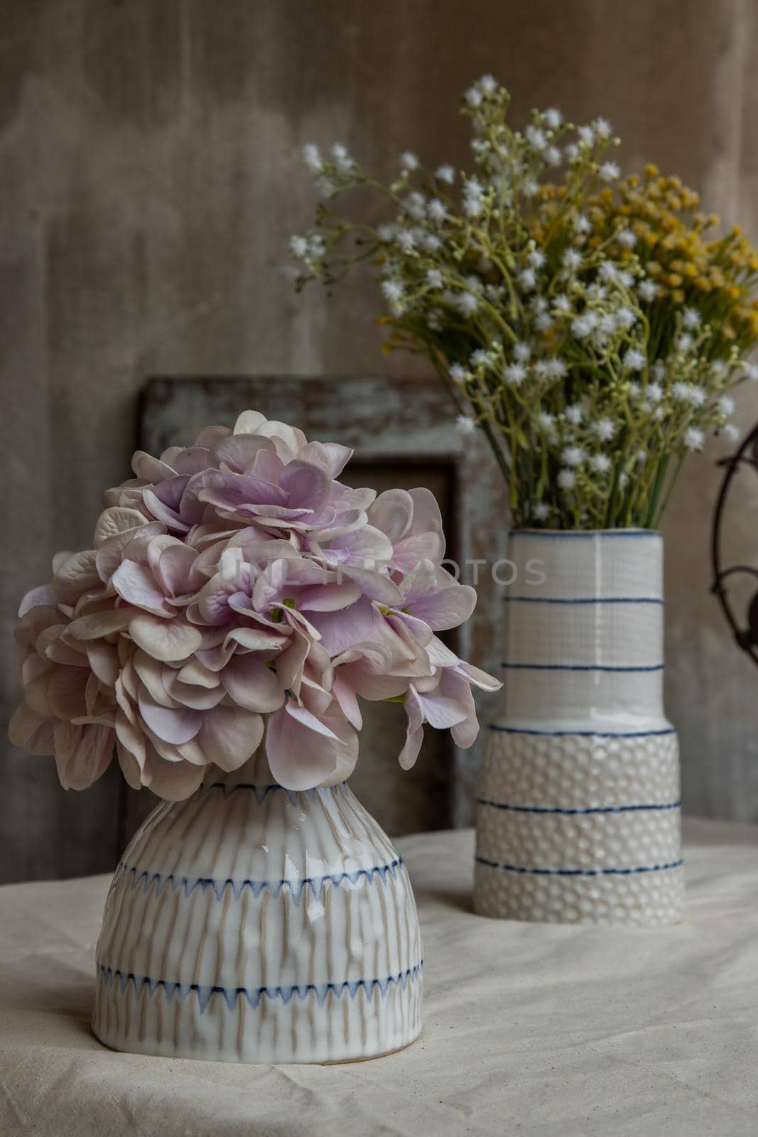 Bouquet of flowers in Two white handmade ceramic vase on white textured table cloth with old cement wall at the balcony house. Home decor, Selective focus.
